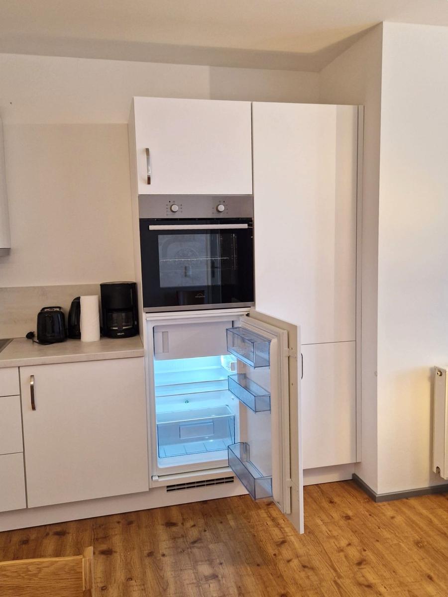 Weiße Küche mit Backofen und geöffnetem, beleuchtetem Kühlschrank.