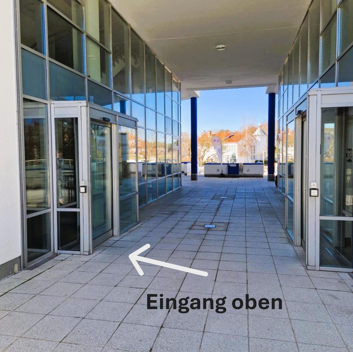 Überdachter Durchgang zwischen Glasfronten mit Schiebetüren.