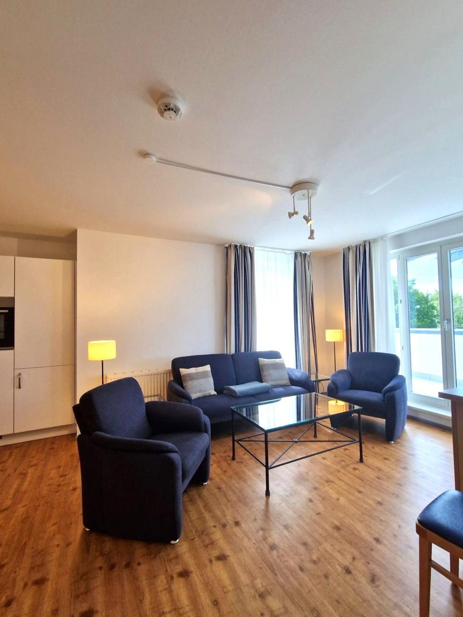 Wohnzimmer mit blauem Sofa, zwei Sesseln, Glastisch und Balkontür.