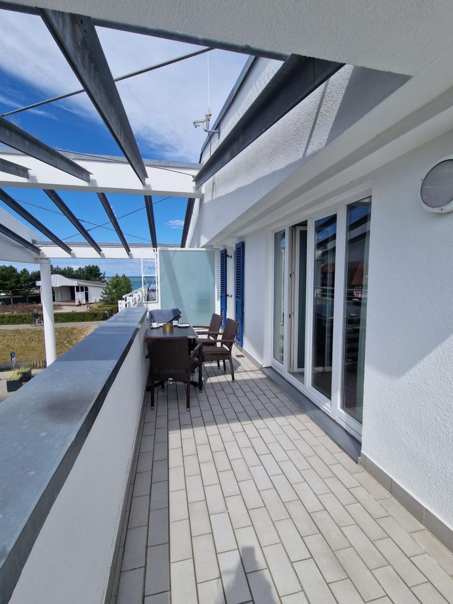 Langer Balkon mit Fliesen, Korbmöbeln, blauen Fensterläden und Pergola.