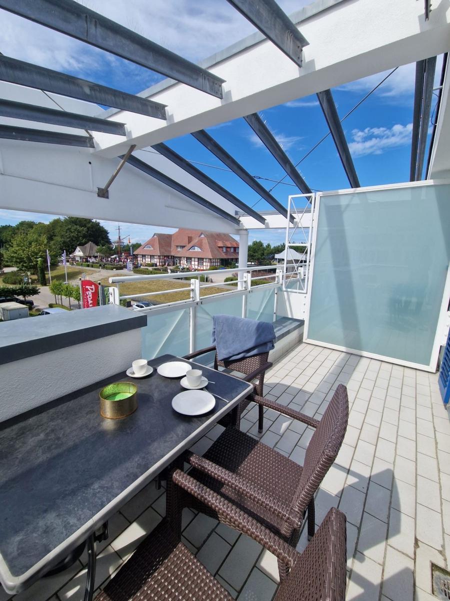 Balkon mit Esstisch, Korbstühlen, Pergola und Blick auf Bäume.