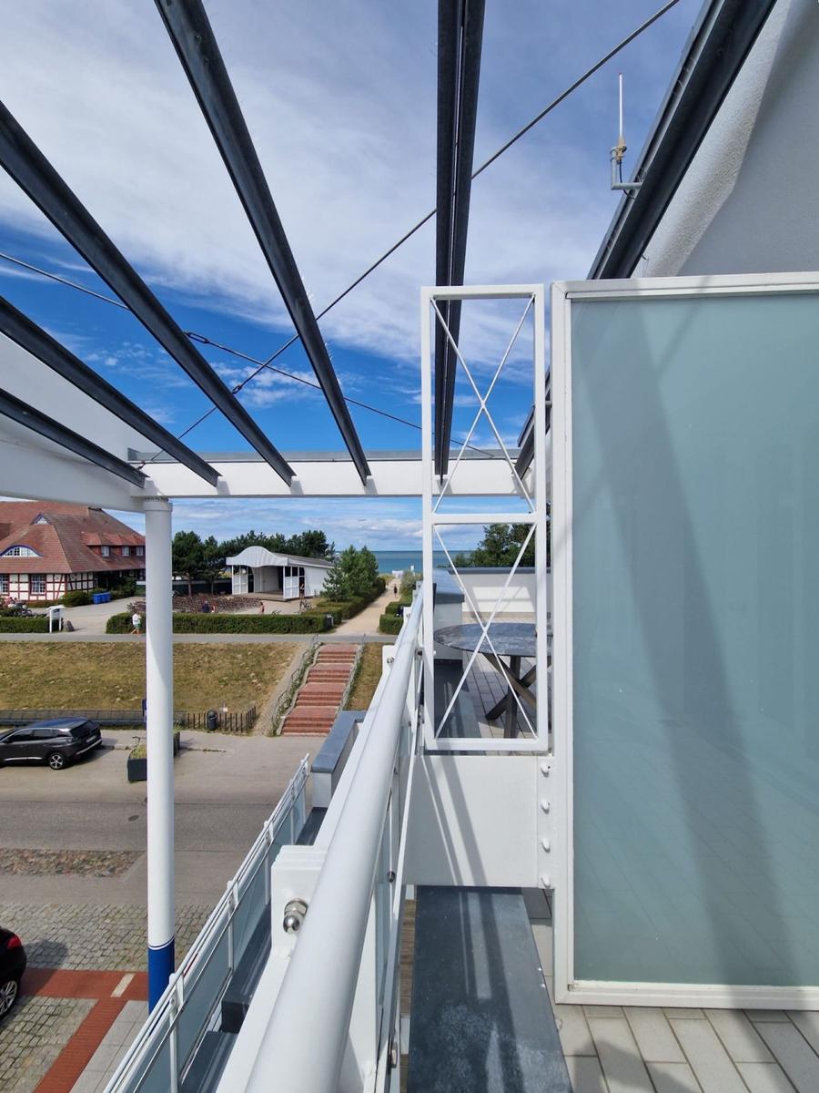 Blick vom Balkon über Straße, Fachwerkhaus und Bäume zum Meer.