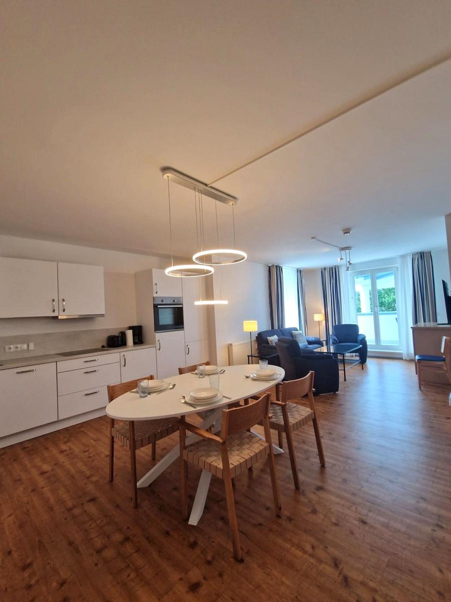 Offener Wohnraum mit Esstisch, Ringlampe, weißer Küche und blauem Sofa.