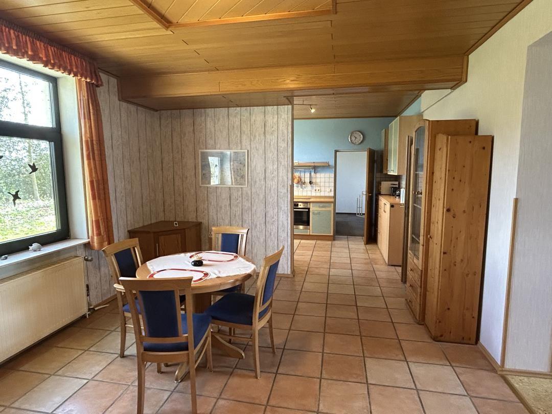 Essbereich mit rundem Holztisch, blauen Stühlen und offener Küche.
