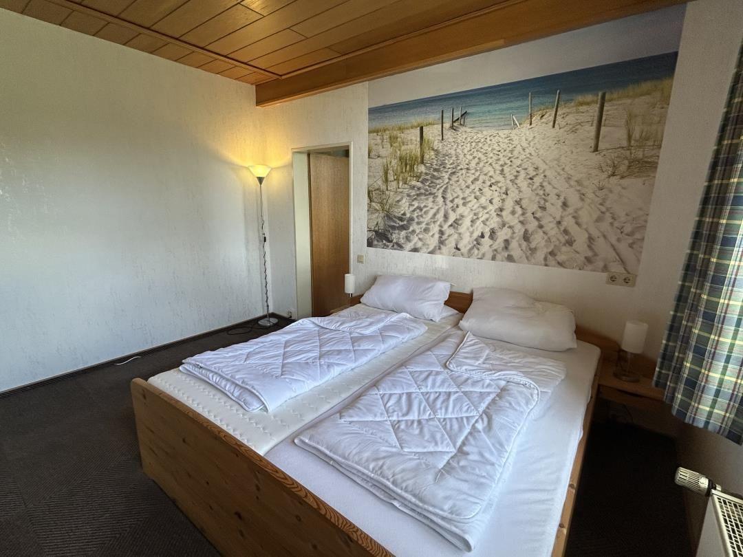 Schlafzimmer mit Doppelbett, Strand-Fototapete und Holzdecke.