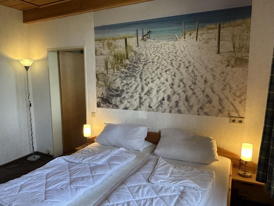 Schlafzimmer mit Doppelbett, weißem Bezug und Strand-Wandbild am Kopfteil.