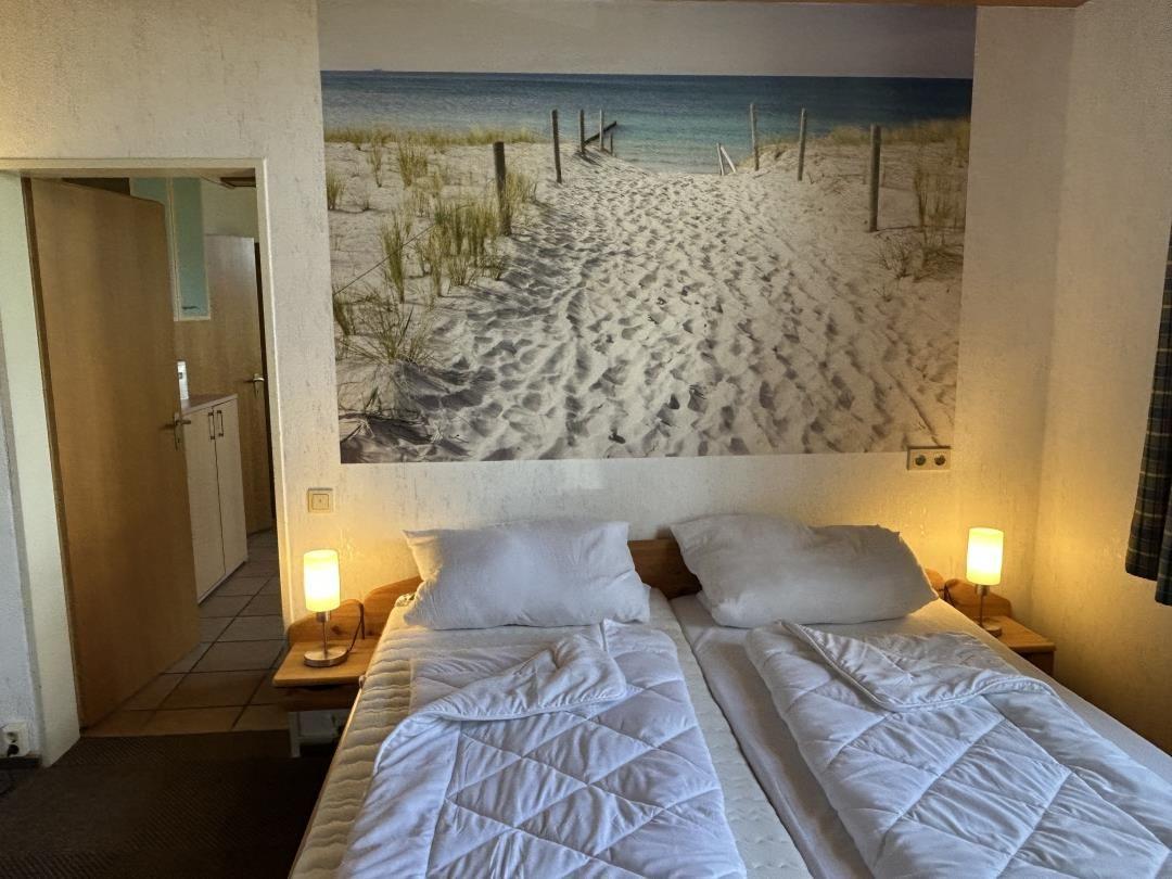 Schlafzimmer mit Doppelbett, Nachttischlampen und Wandbild mit Dünenweg.