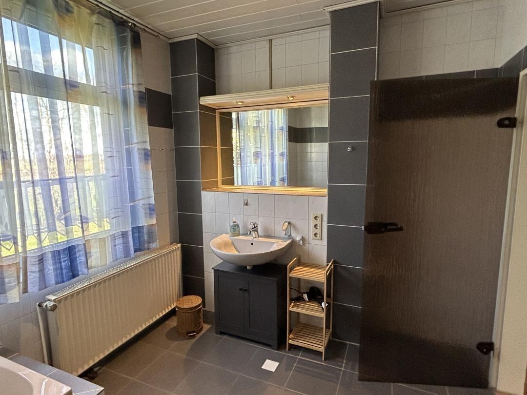 Badezimmer mit Waschbecken, Spiegel, gemustertem Fenstervorhang und Heizkörper.