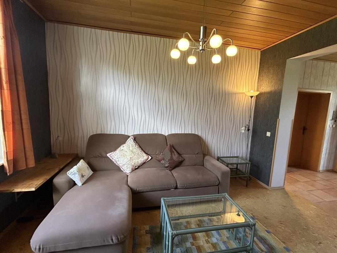 Braunes Ecksofa vor weißer Wellenwand, Glastisch und Holzdecke.
