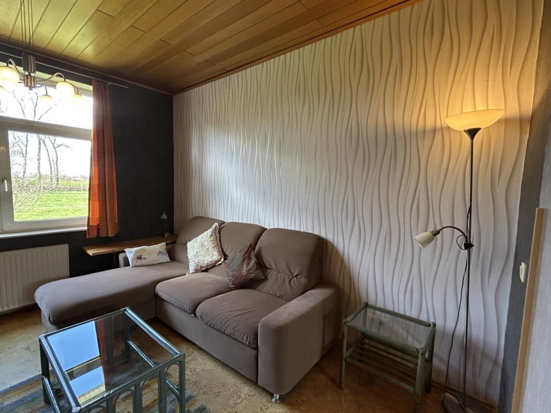 Braunes Ecksofa mit Glastischen, Stehlampe und orangem Vorhang.