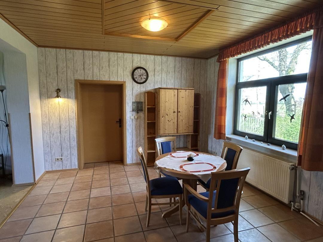 Essbereich mit rundem Holztisch, blauen Stühlen, Schrank und Fenster.