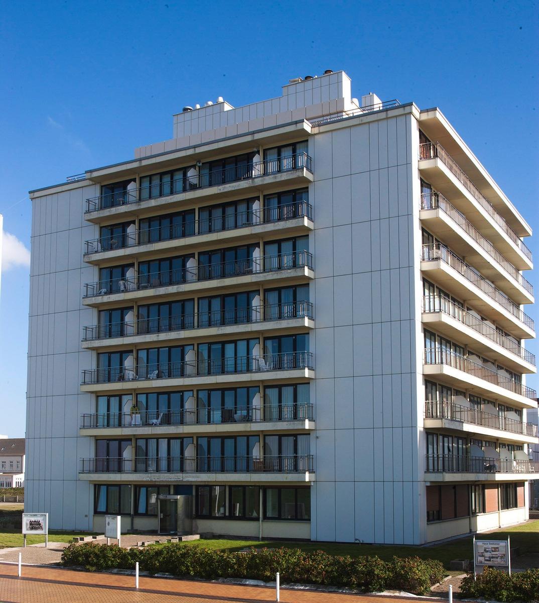 Mehrstöckiges weißes Apartmenthaus mit vielen Balkonen vor blauem Himmel.