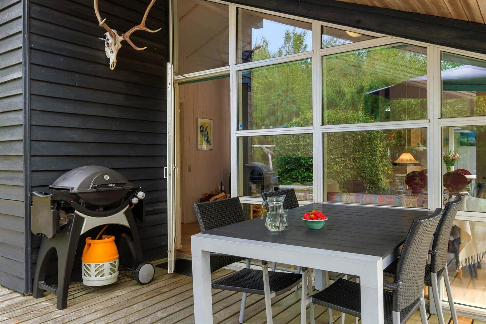 Holzterrasse mit Esstisch, vier schwarzen Stühlen, Gasgrill und Geweih an der Wand.