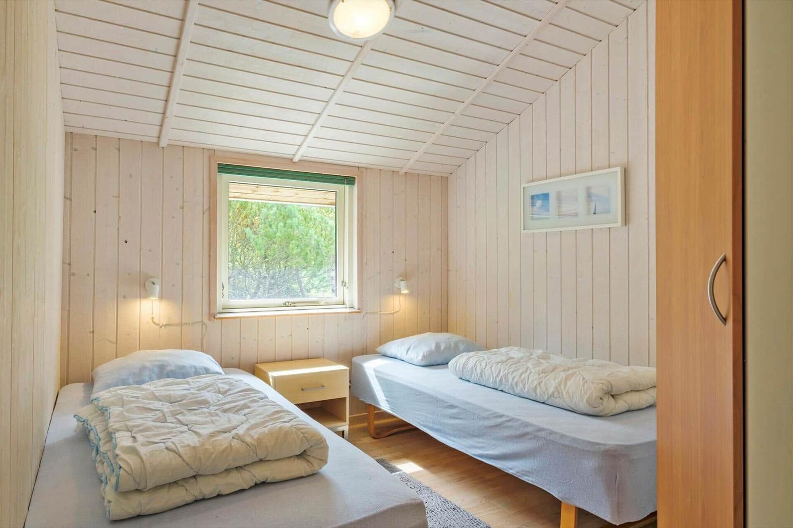 Schlafzimmer mit zwei Einzelbetten, Nachttisch und Fenster mit Blick ins Grüne.