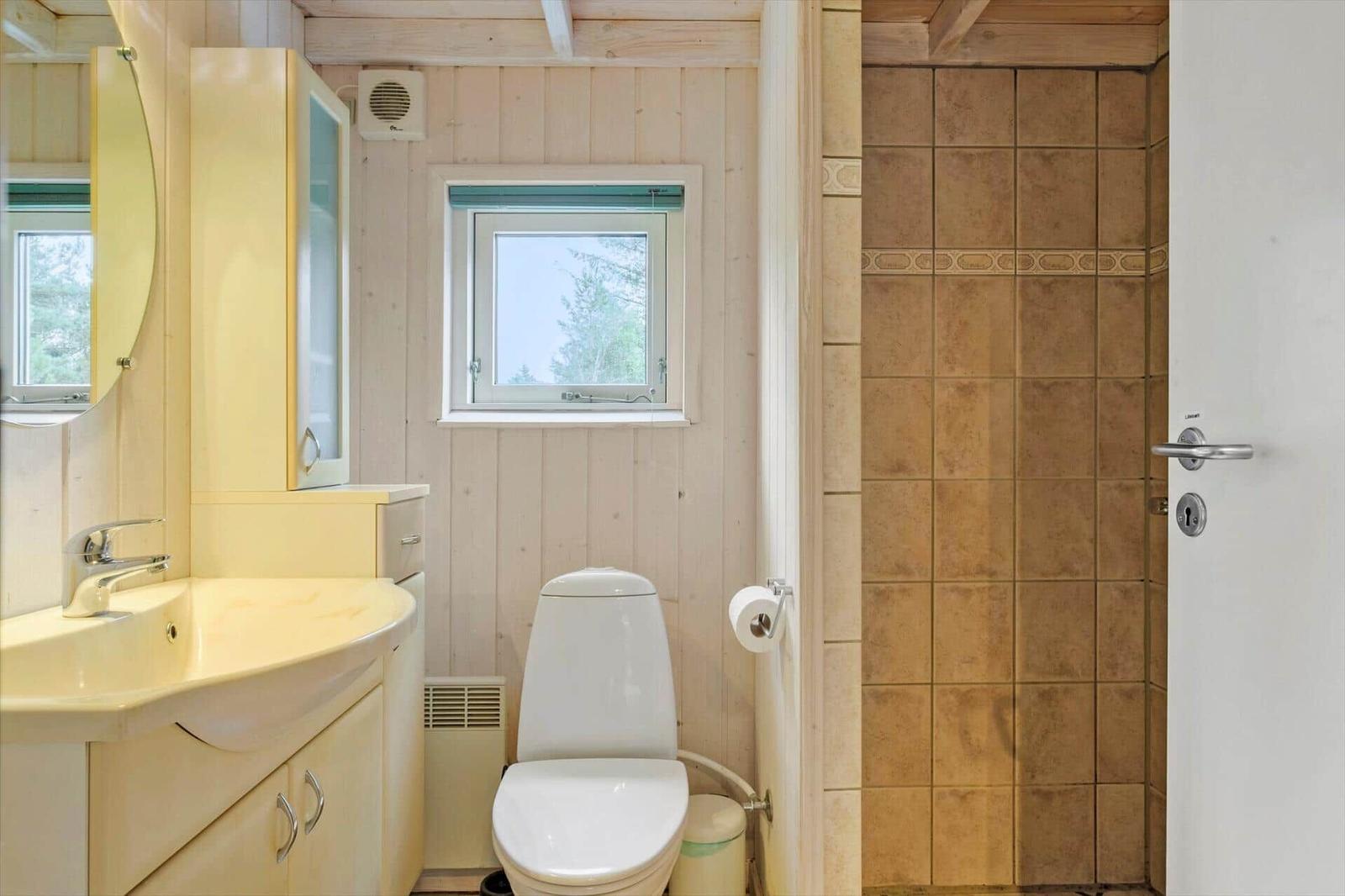 Badezimmer mit Waschtisch, WC, Fenster und Dusche mit braunen Fliesen.