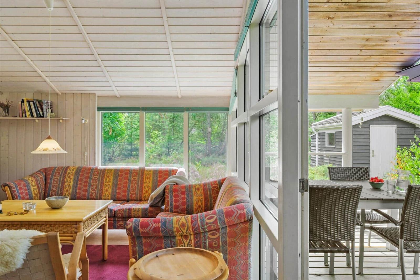 Wohnzimmer mit buntem Sofa, Couchtisch und Blick auf Terrasse mit Gartenhaus.