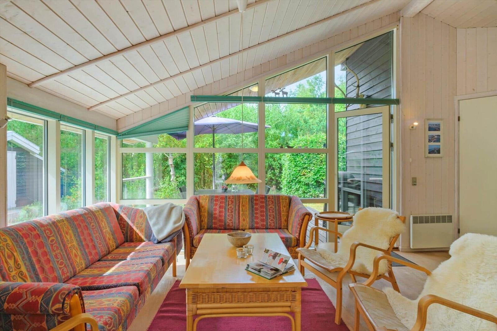 Wohnzimmer mit zwei Sofas, Sesseln, Couchtisch und Fensterfront zum Garten.