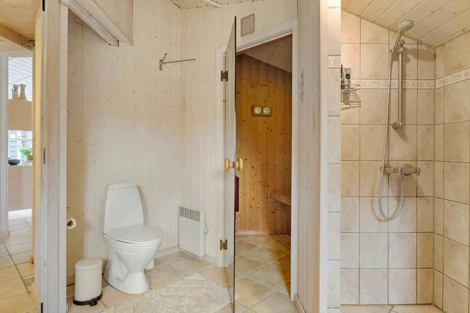 Bad mit WC, beiger Dusche und offener Glastür zur Holzsauna.