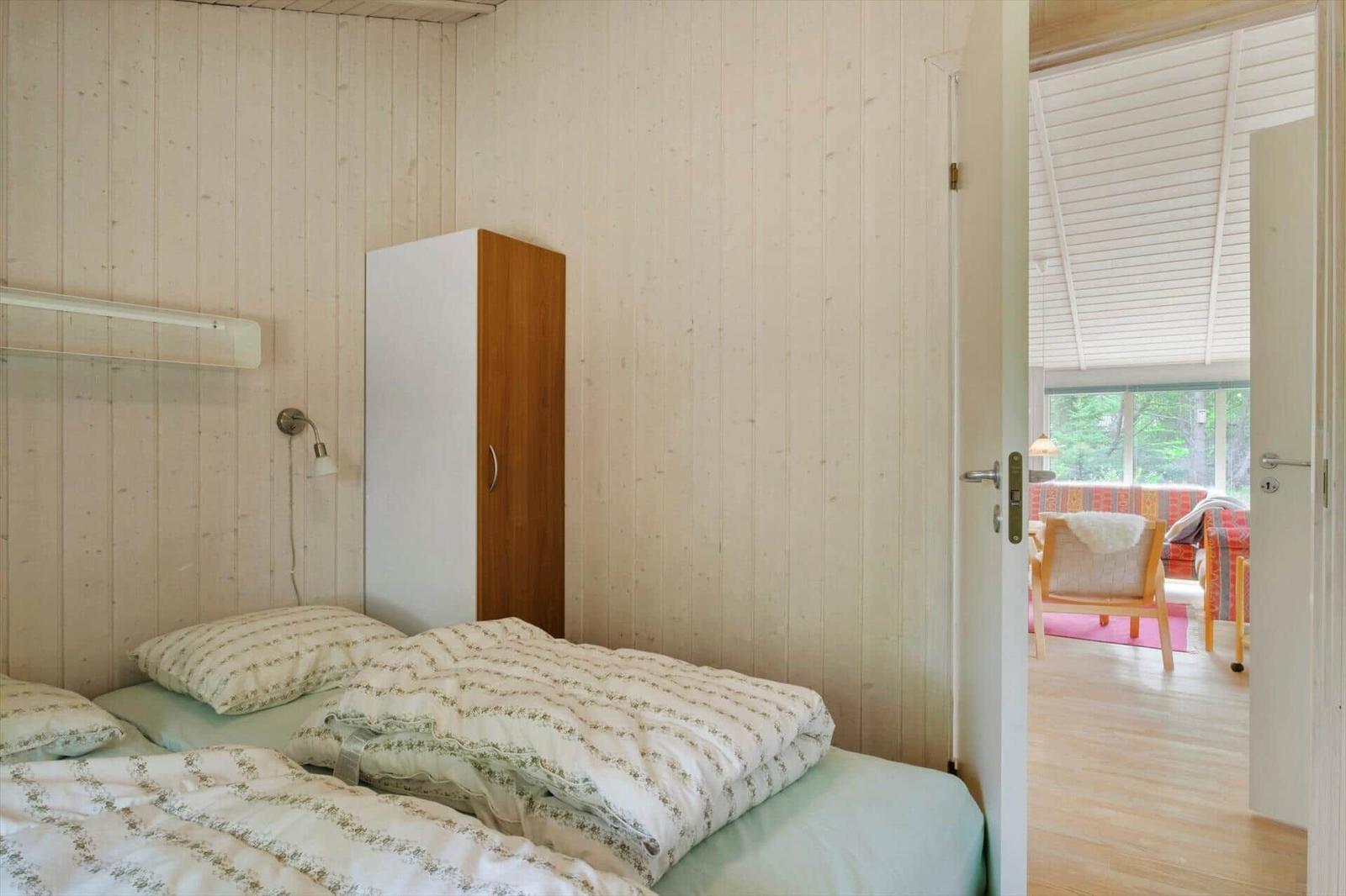Schlafzimmer mit Bett, Schrank und Blick durch offene Tür ins Wohnzimmer.
