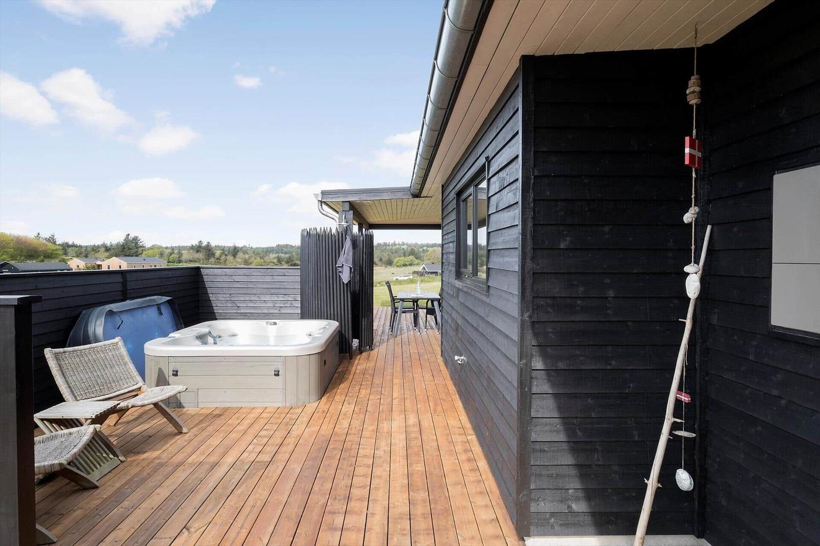Holzterrasse mit Whirlpool, Korbstühlen und Blick in die Landschaft.