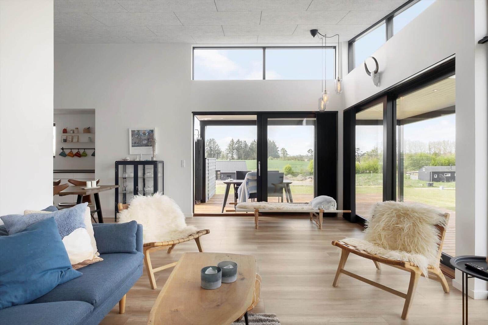 Heller Wohnraum mit blauem Sofa, Fellsesseln, Holzliege und Glasfront zur Terrasse.