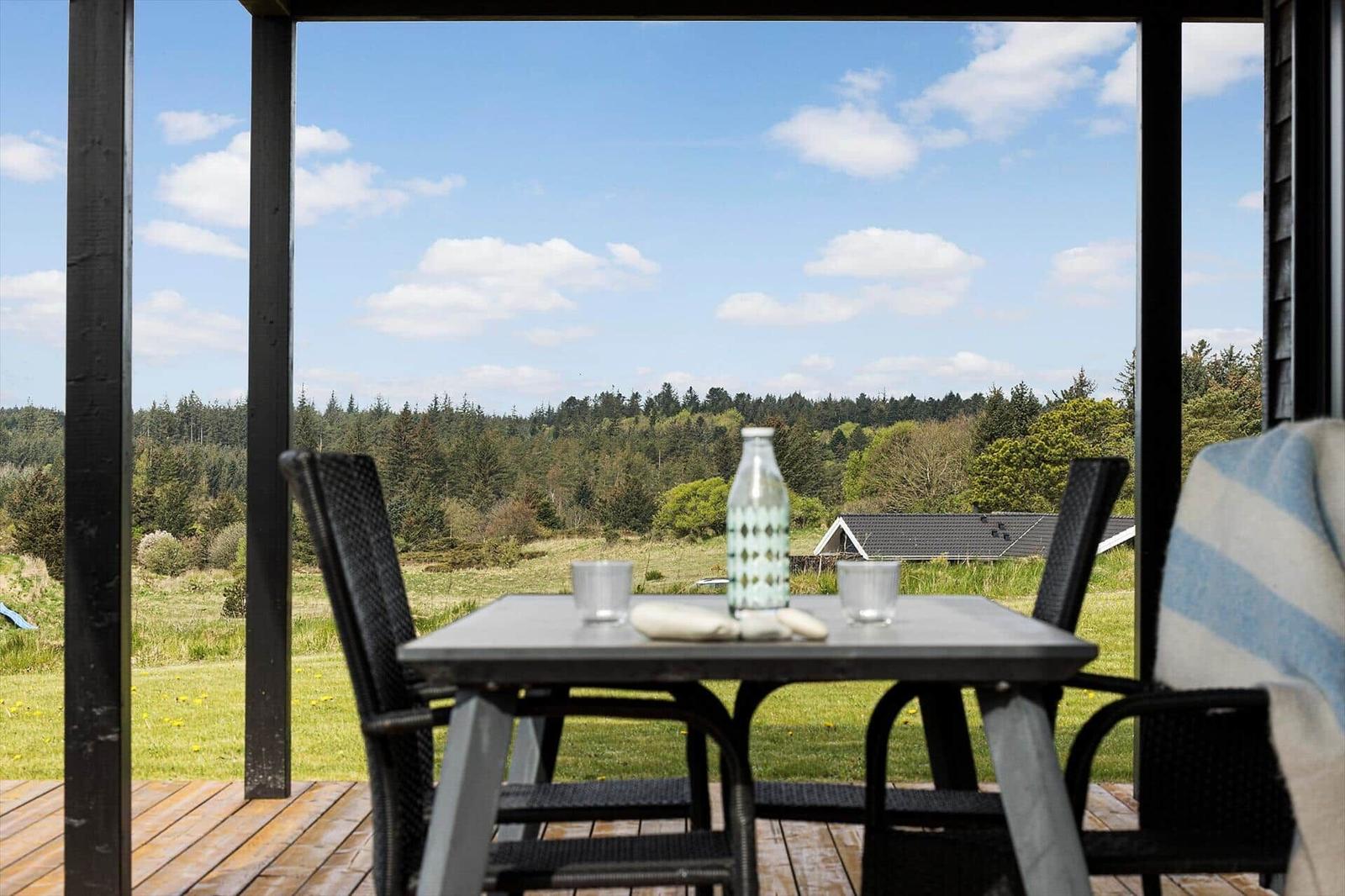 Überdachte Holzterrasse mit Esstisch, Rattanstühlen und Blick über die Wiese zum Wald.