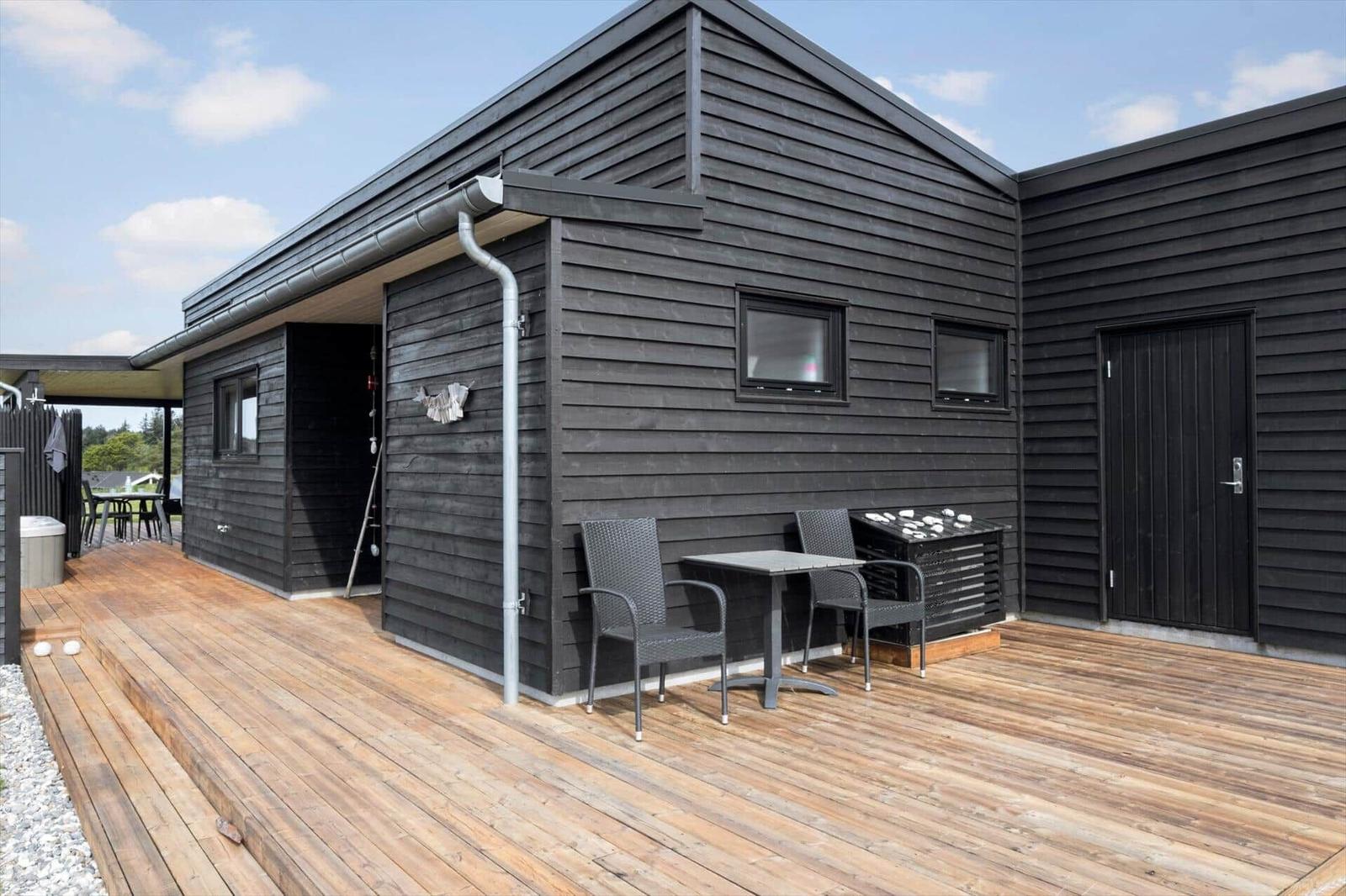 Holzterrasse mit zwei Rattansesseln und kleinem Tisch vor schwarzer Holzfassade.