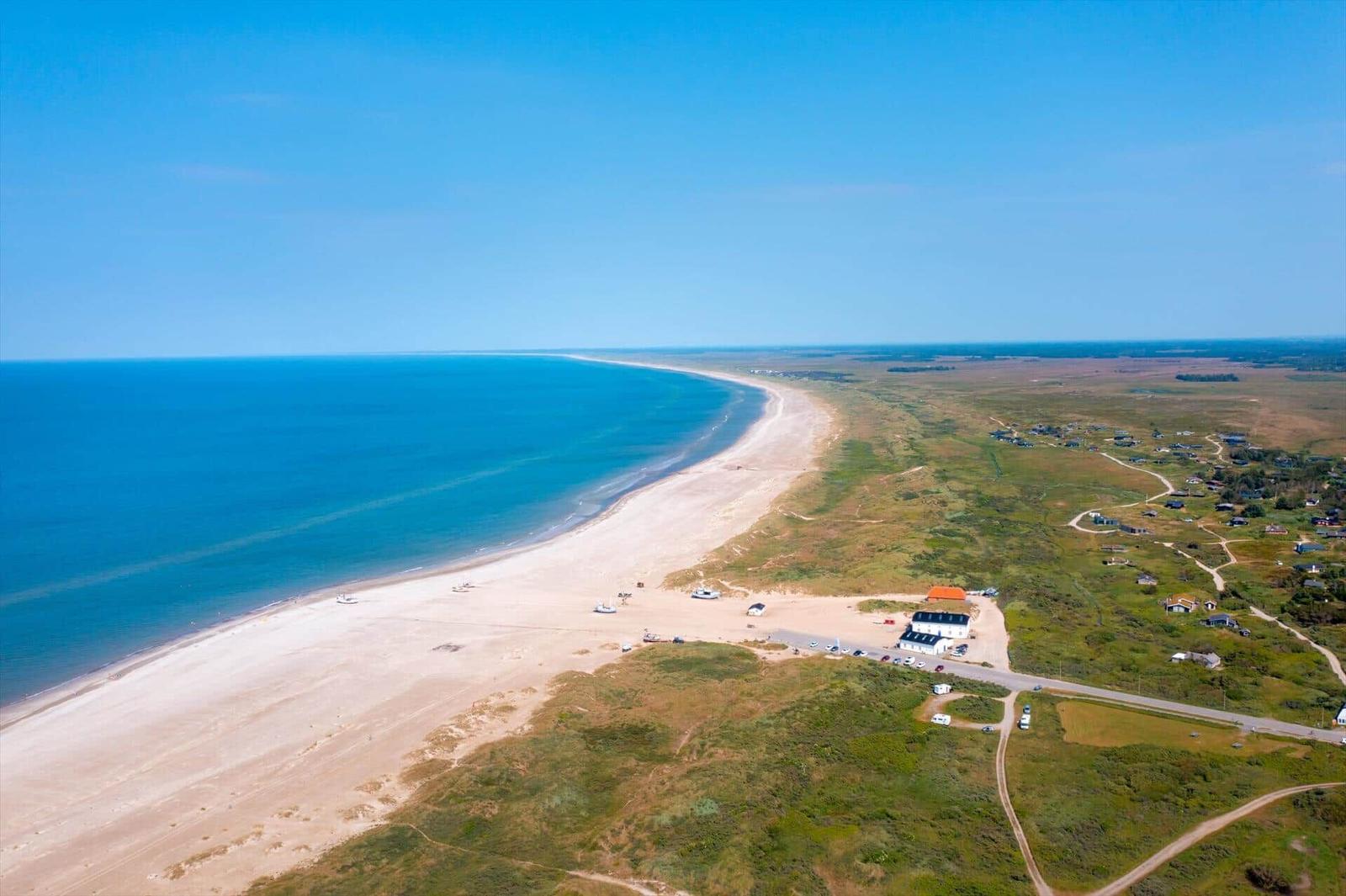 Luftbild von Sandstrand, Dünenbewuchs, Meer und Häusern an der Küste.