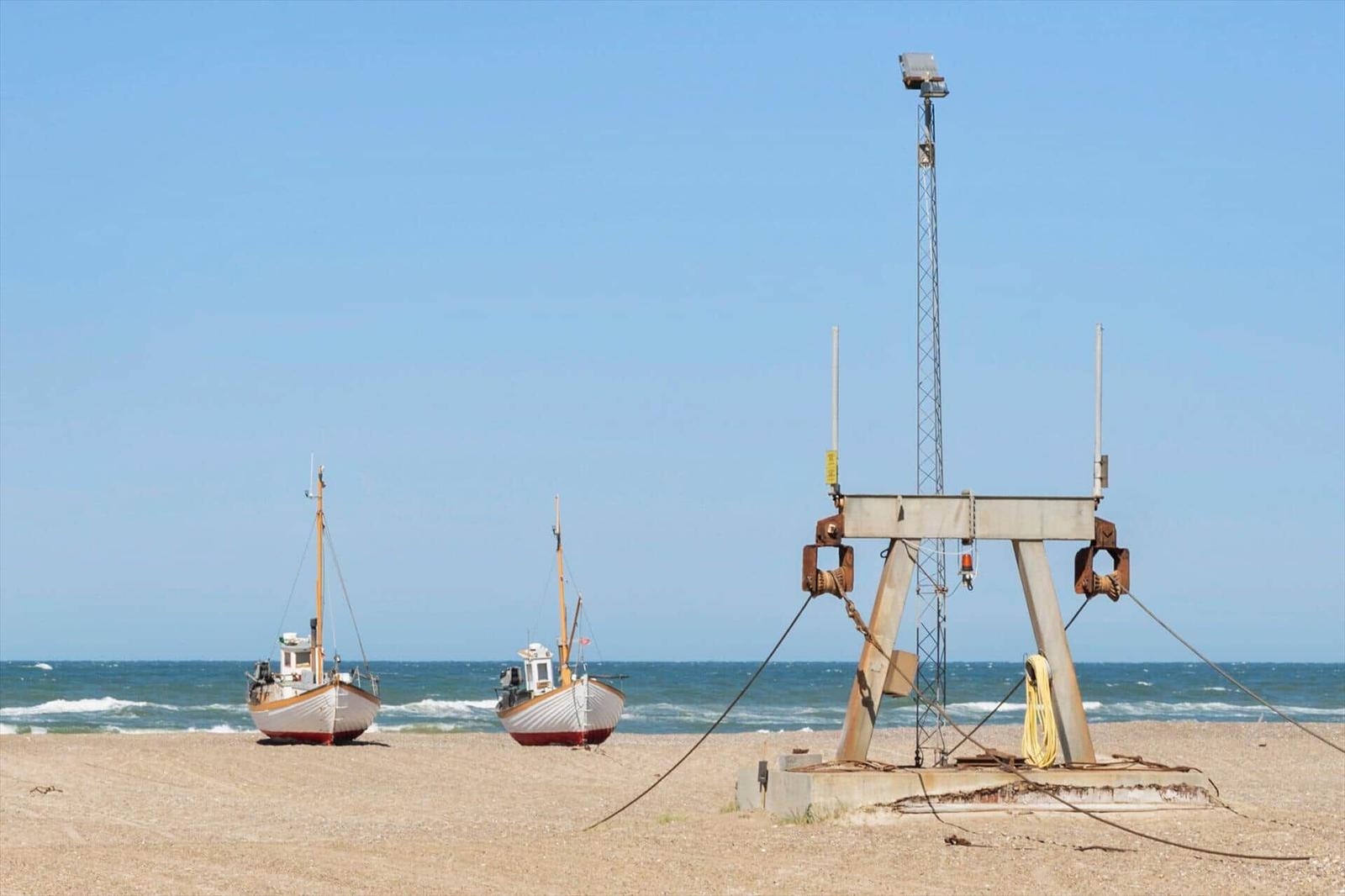 Zwei Fischerboote am Sandstrand vor blauem Meer mit Metallwinde und Mast.
