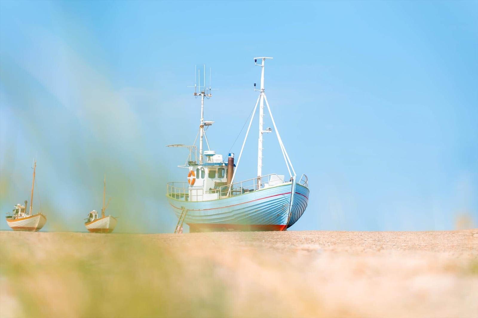 Hellblaues Fischerboot mit weißem Aufbau auf Sandstrand unter klarem Himmel.