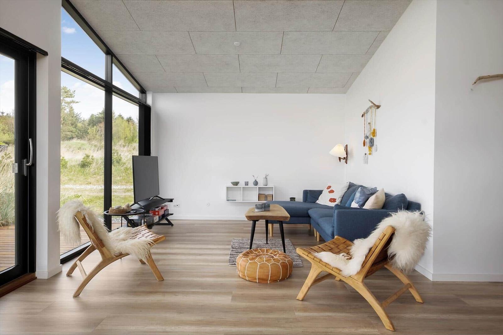 Wohnzimmer mit blauem Ecksofa, Holzstühlen und großer Fensterfront.