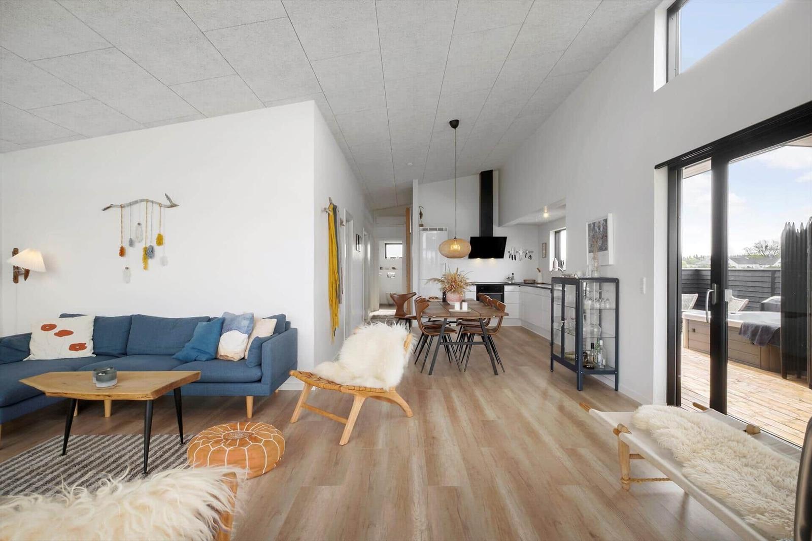 Wohnraum mit blauem Sofa, Esstisch, Küche und Terrasse mit Whirlpool.
