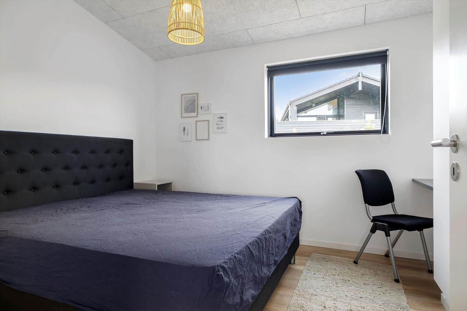 Schlafzimmer mit Doppelbett, gerahmten Bildern, Schreibtisch und Korblampe.