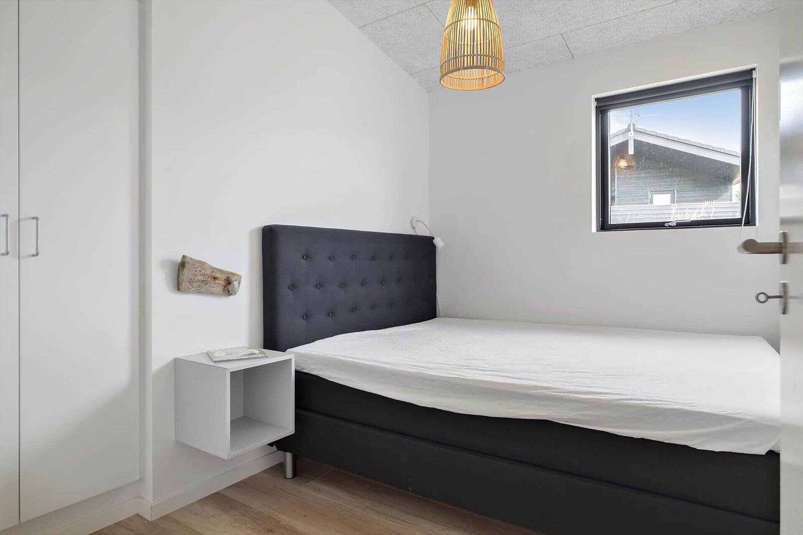 Schlafzimmer mit Doppelbett, dunklem Kopfteil und weißem Hängenachttisch.
