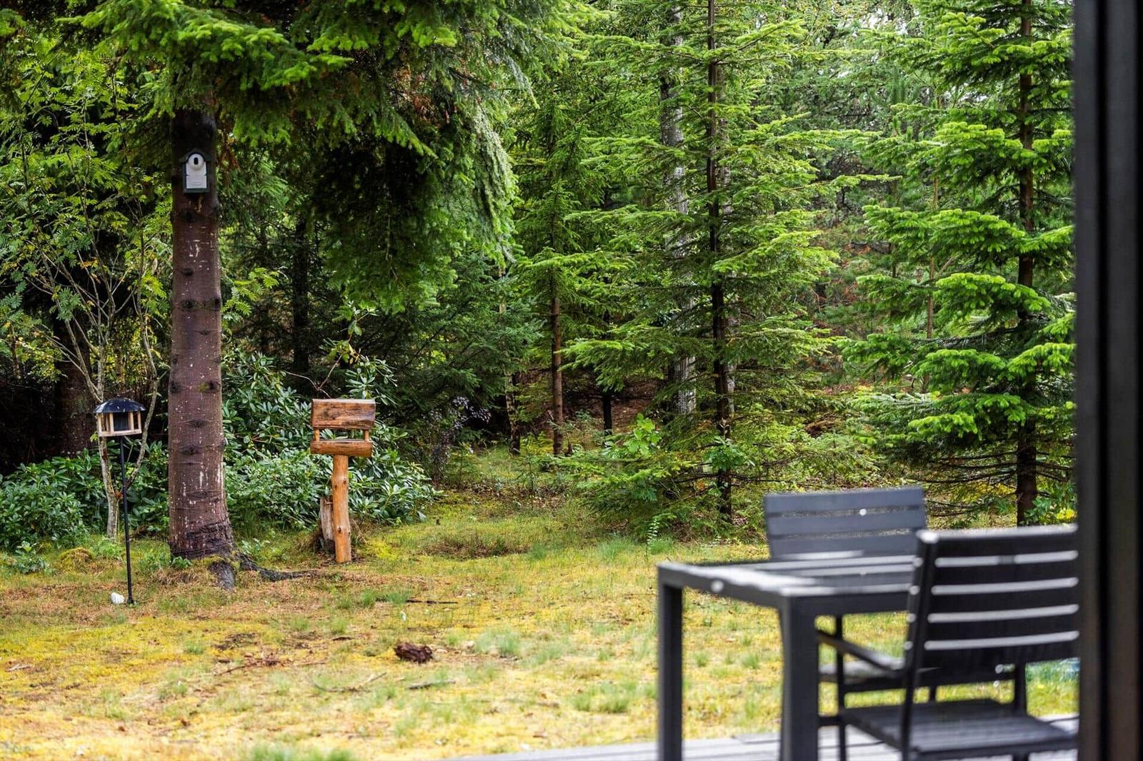 Wooden terrace with garden furniture facing a wooded garden with birdhouses.