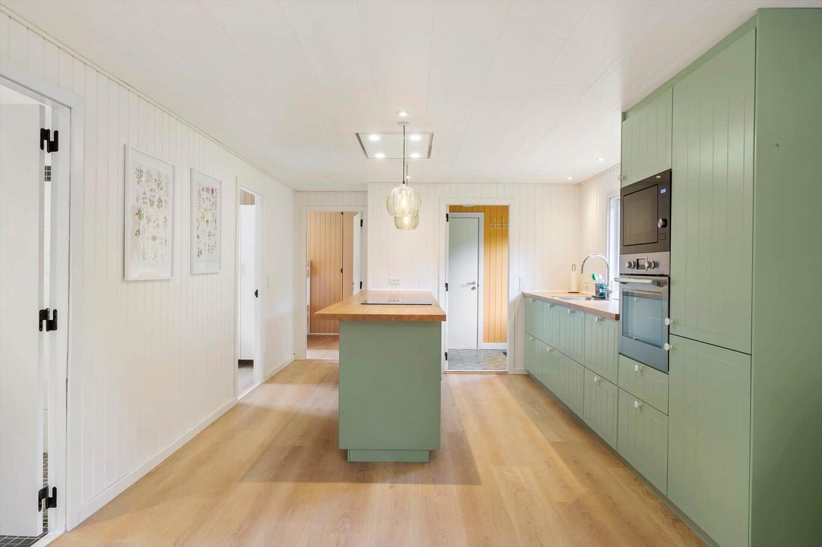 Open kitchen with grooved green cabinets, island and hallway doorways.