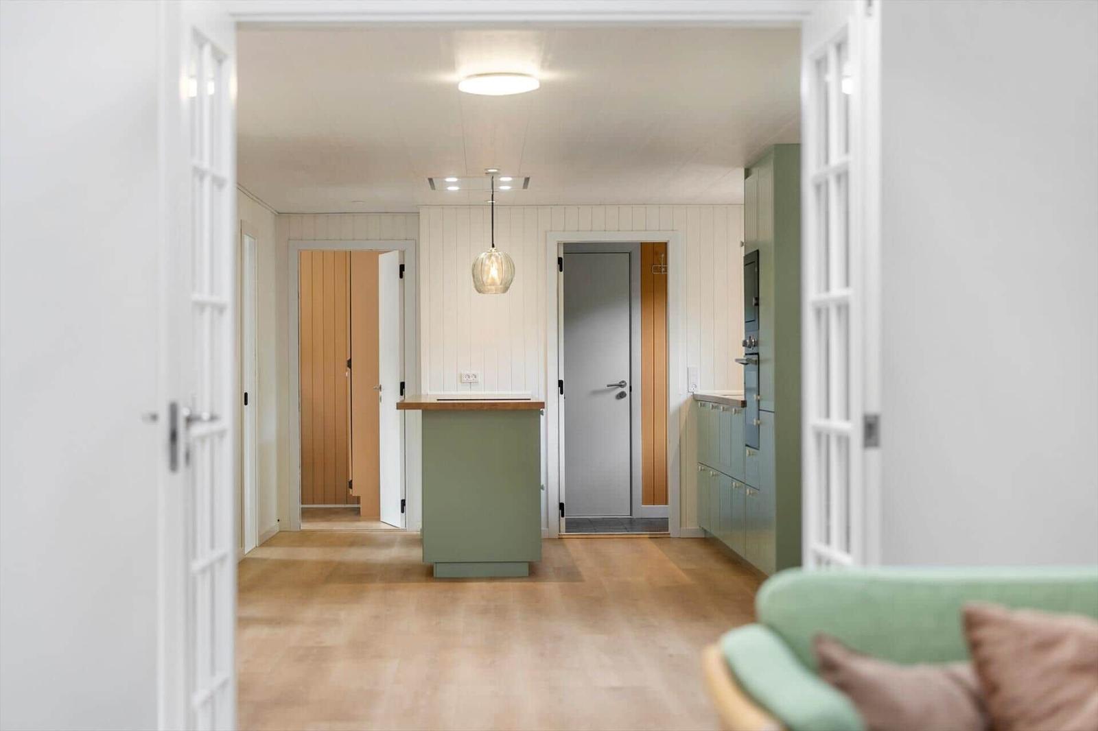 View through white glass doors to a green kitchen island and wood walls.