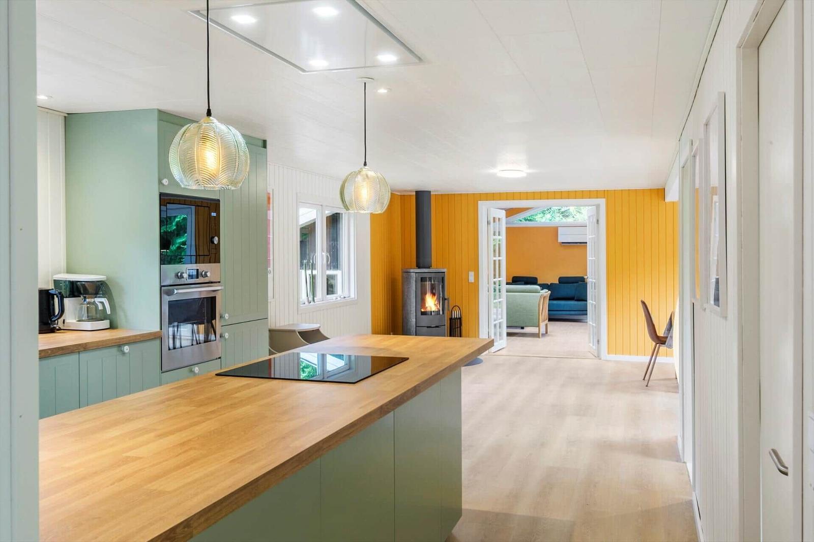 Kitchen with island, wood stove and yellow wood wall towards the living area.