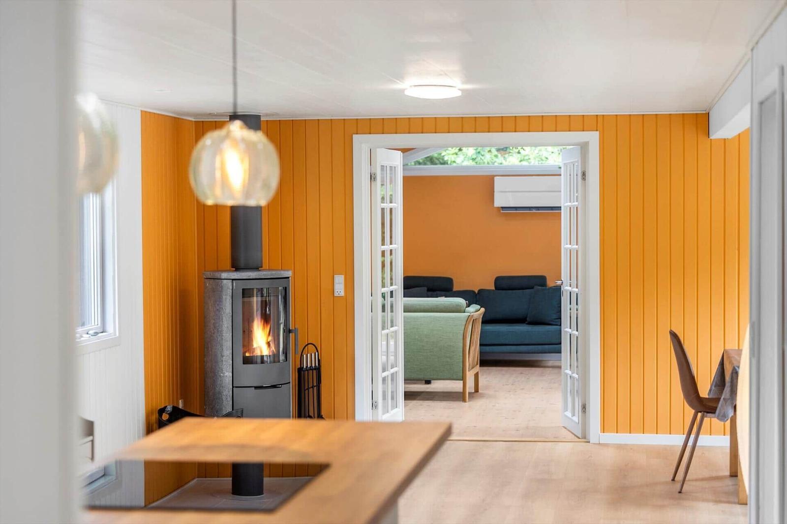 Living area with lit wood stove, yellow wood walls and view into next room.
