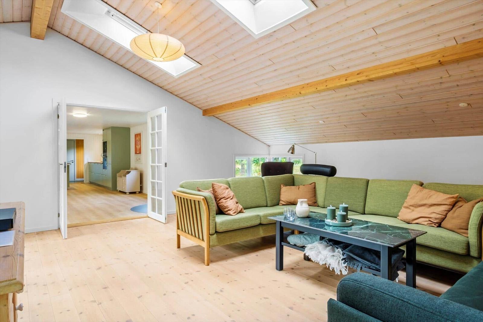 Living area with green corner sofa, coffee table and wood ceiling with skylight.