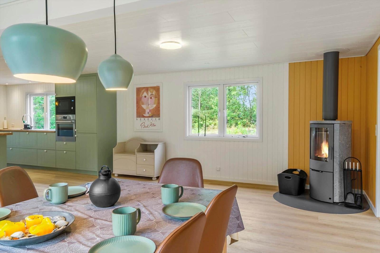 Set dining table near a wood stove and an open kitchen with green cabinets.