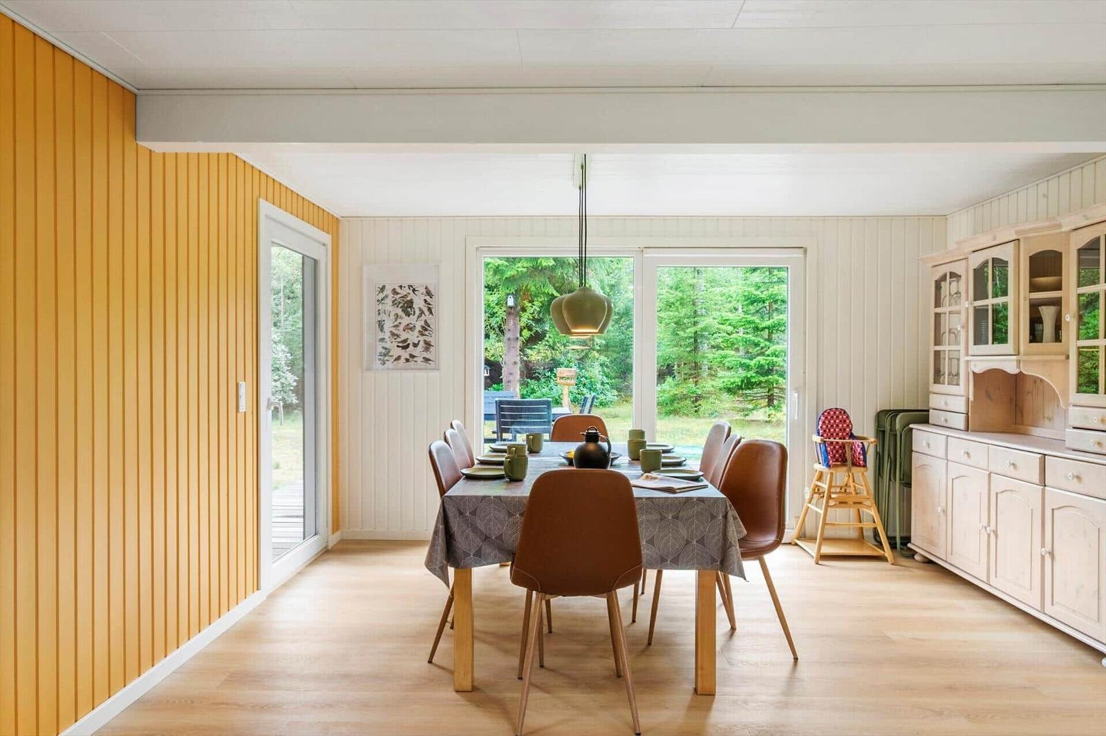 Dining table with brown chairs, wooden sideboard and glass door to the garden.