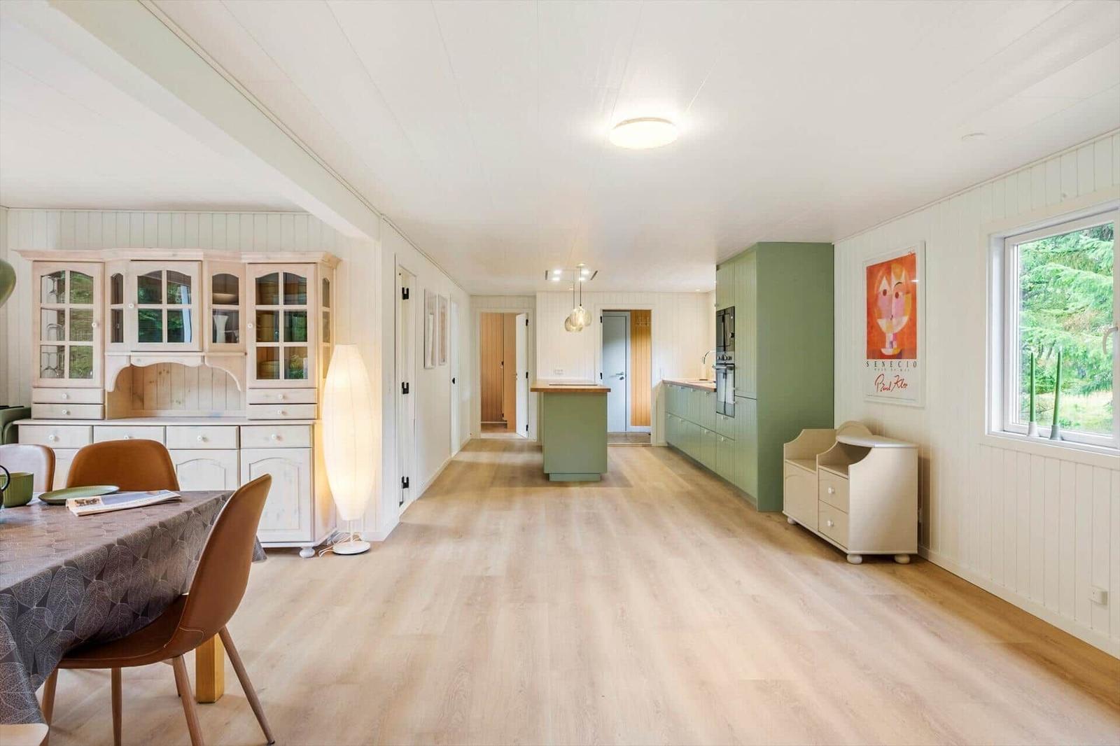 Open living space with wooden buffet, kitchen island and green cabinets.