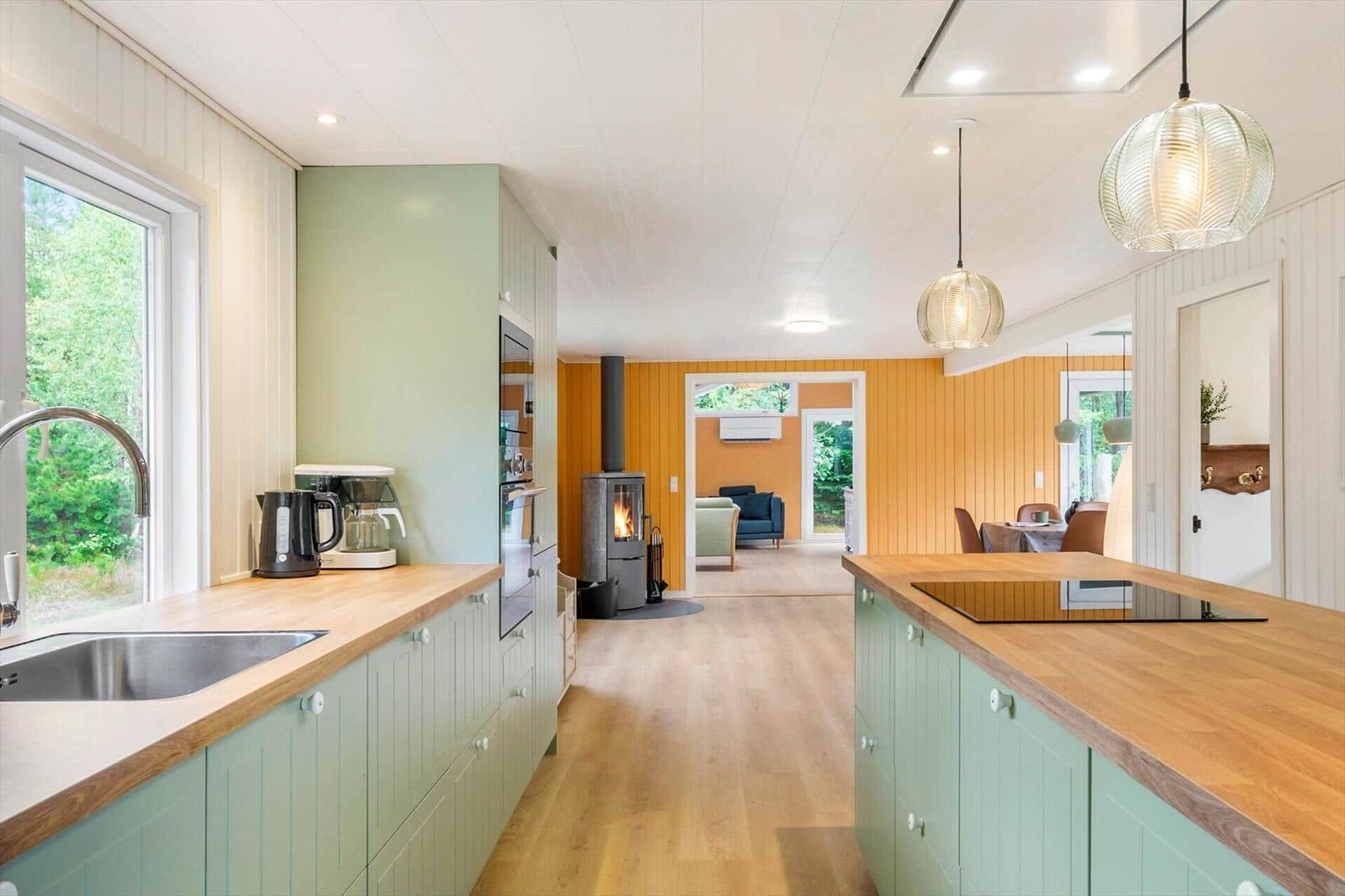 Open kitchen with green cabinets, kitchen island and wood stove in living area.