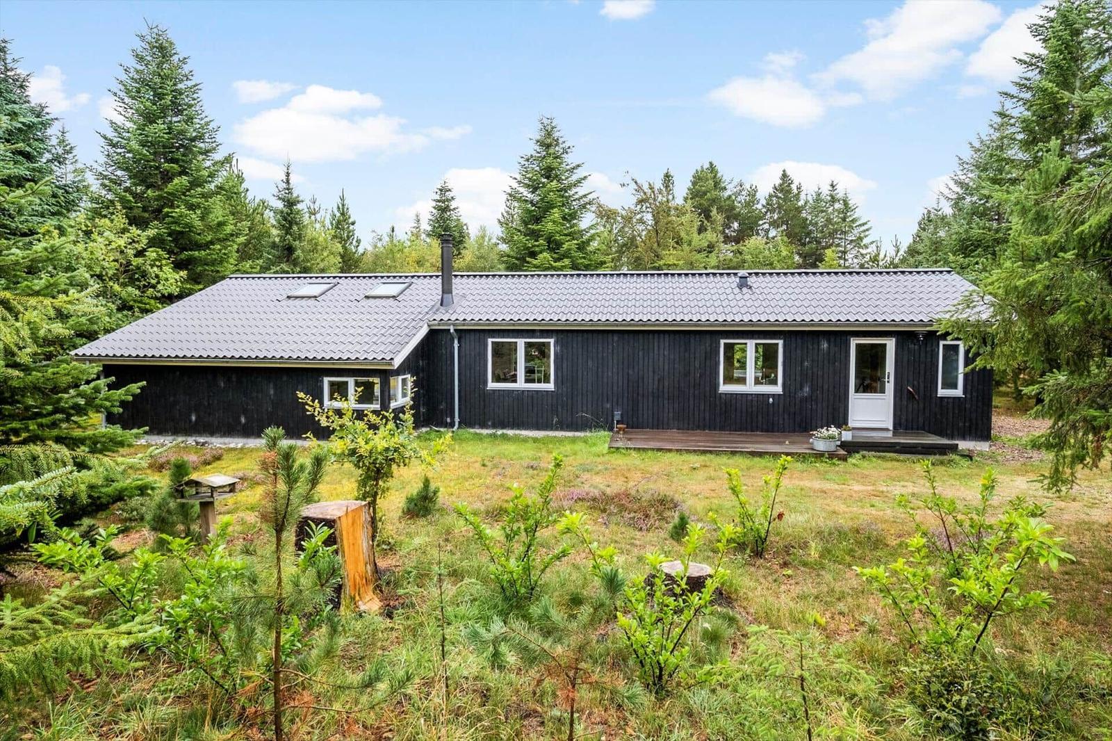 Black wooden house with white door, small terrace and a forest garden.