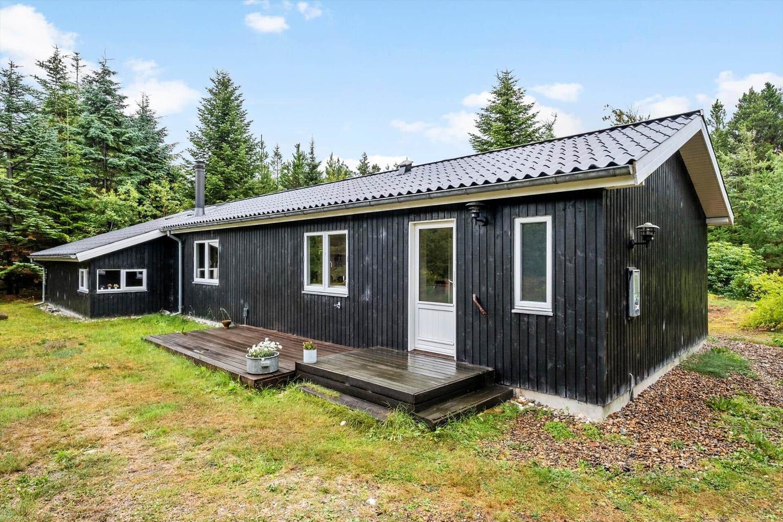 Dark wooden house with white door, stepped terrace and forest grounds.