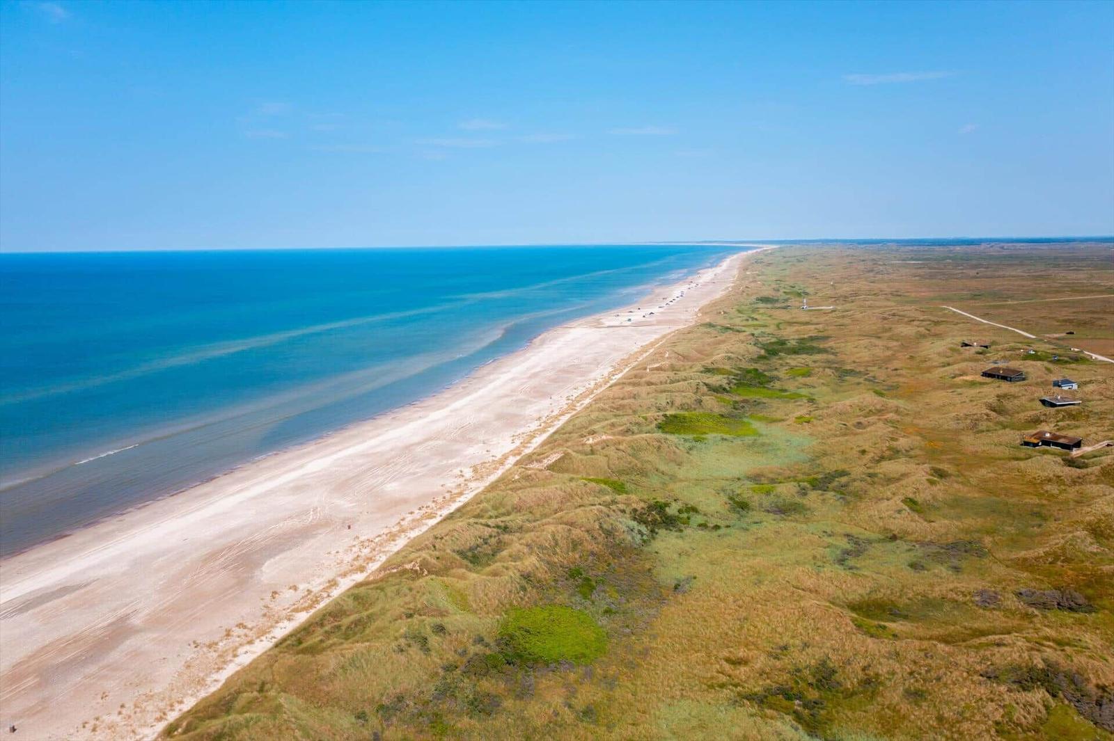 Aerial view of sandy beach, dunes and blue sea under a clear sky.