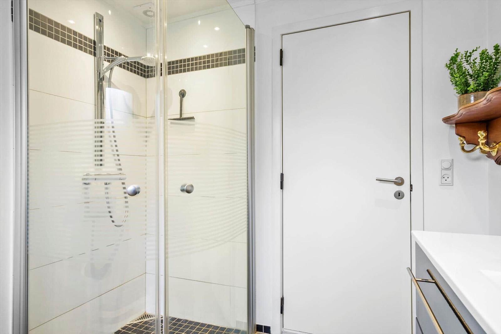 Bathroom with glass shower cabin, white door and wooden wall shelf.