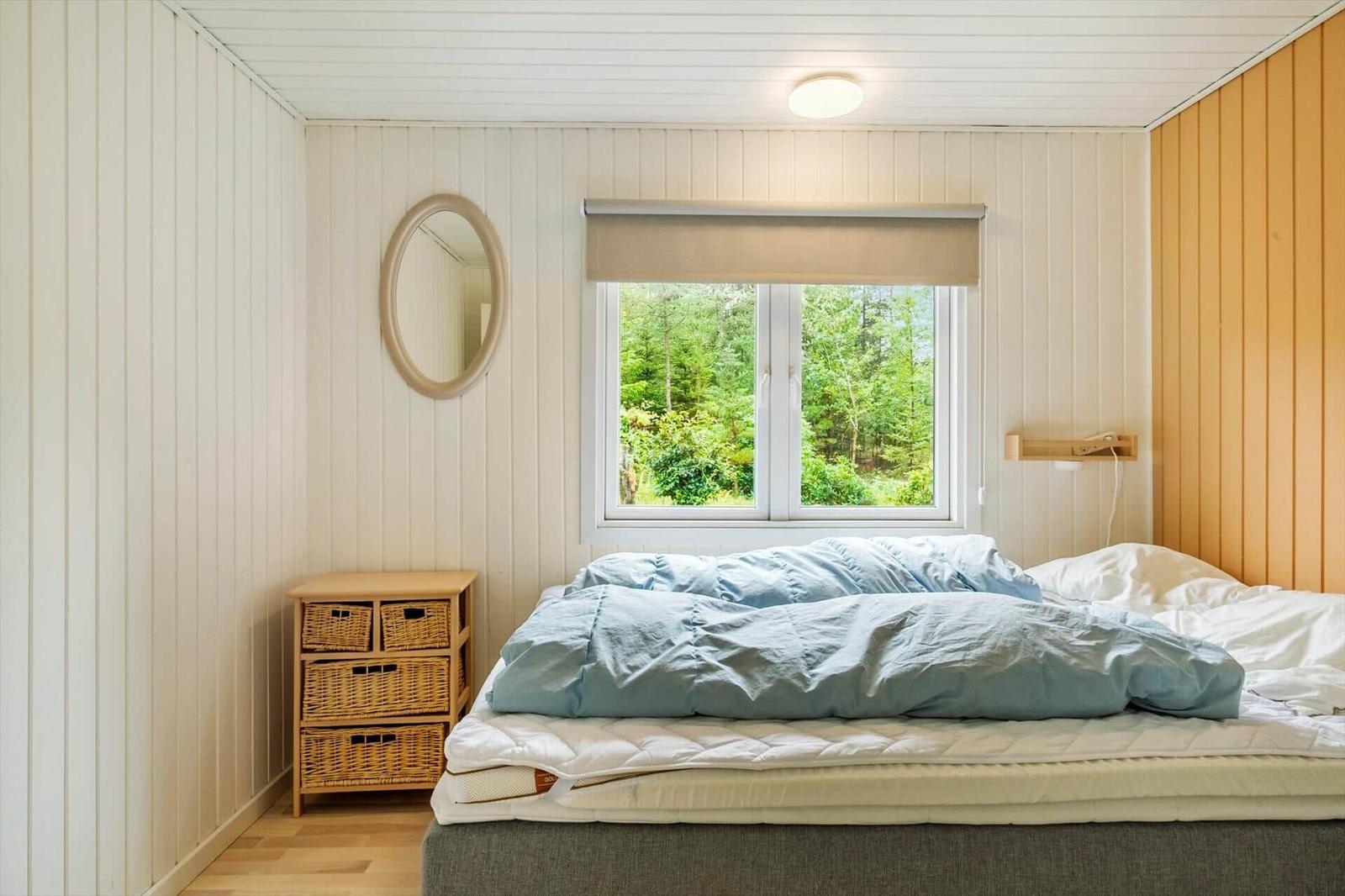 Bedroom with double bed, wicker basket dresser and window view of trees.
