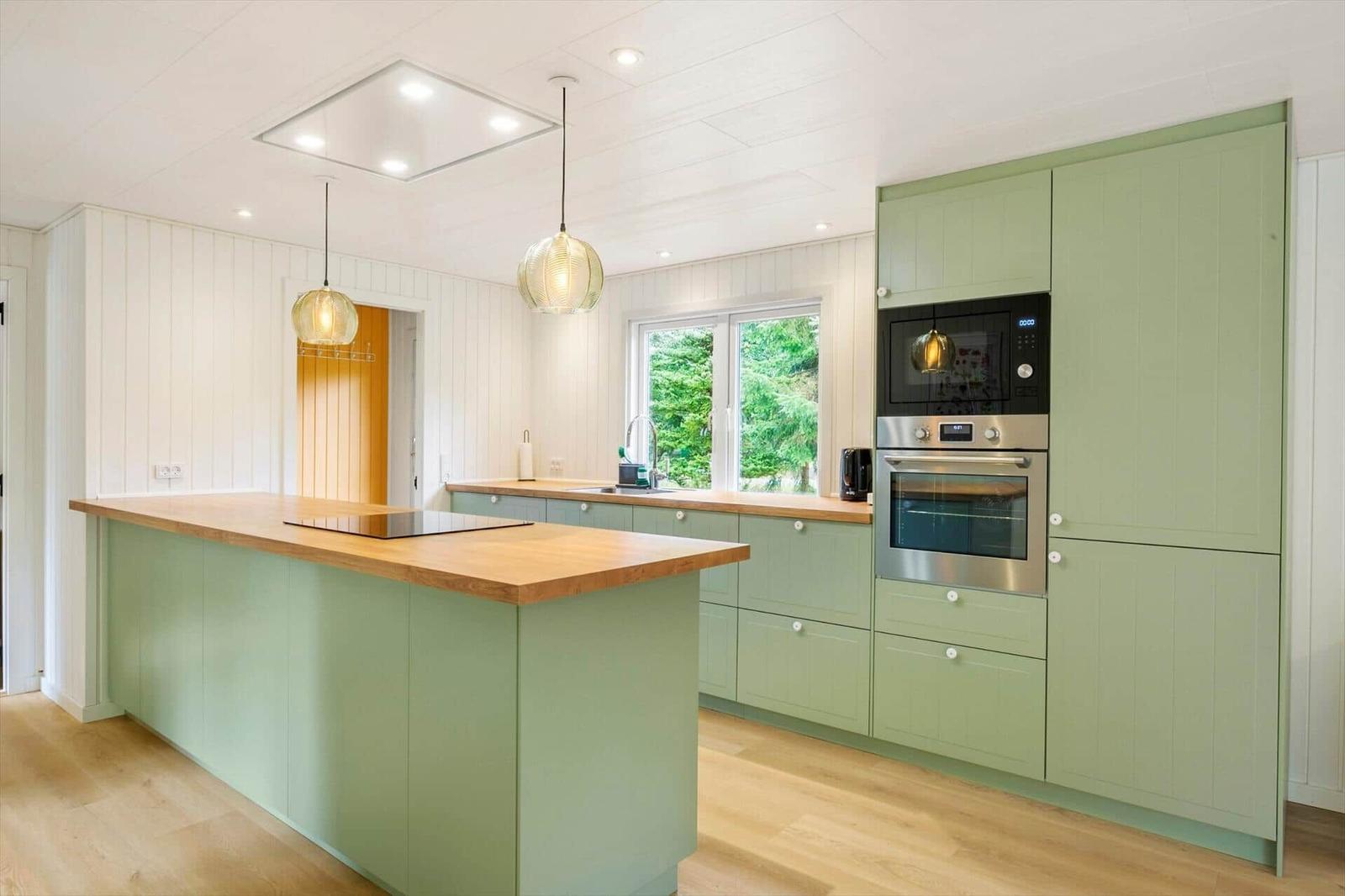 Kitchen with sage green cabinets, island, wooden worktop and built-in appliances.